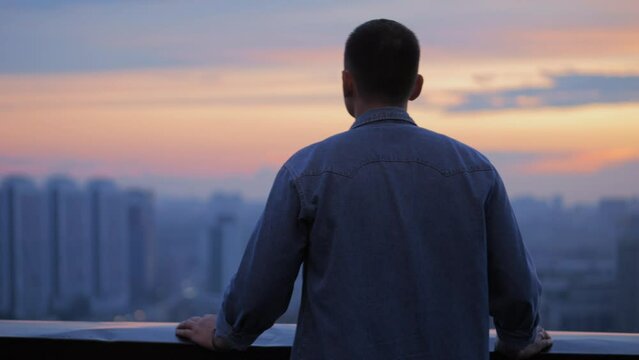 Man on the roof. Guy relax on rooftop. Young guy rest on Roof Terrace. A city view at the sunset time.