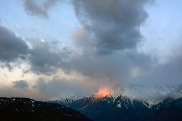 Big winter snowy mountains over which clouds fly by and the evening sun shines. Winter landscape