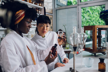 Interracial pharmacists are looking at the cup with liquid medicament