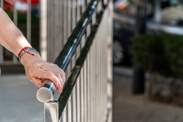 Hands of an elderly woman holding on to the metal railing
