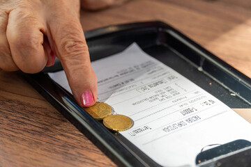 Woman's fingers on euro coins on restaurant bill, tip concept - obrazy, fototapety, plakaty