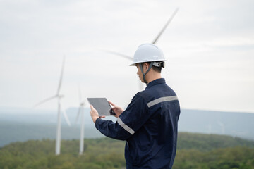 A worker in a wind turbine field looks towards the sky while holding a tablet, managing the efficient production of renewable energy.