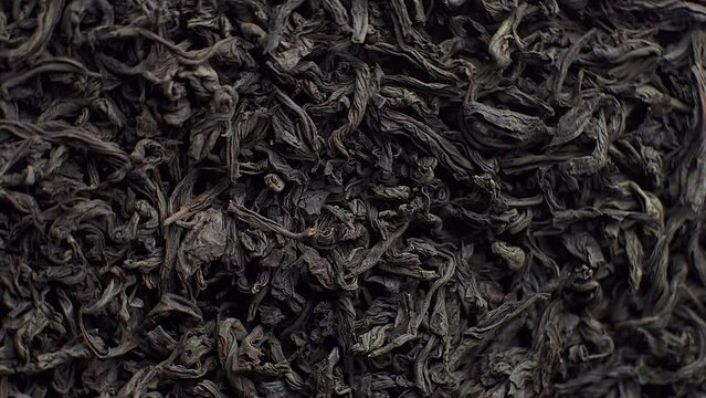Background for a cafe or restaurant, black loose leaf tea sprinkled on a plate and spinning close up, tea advertising