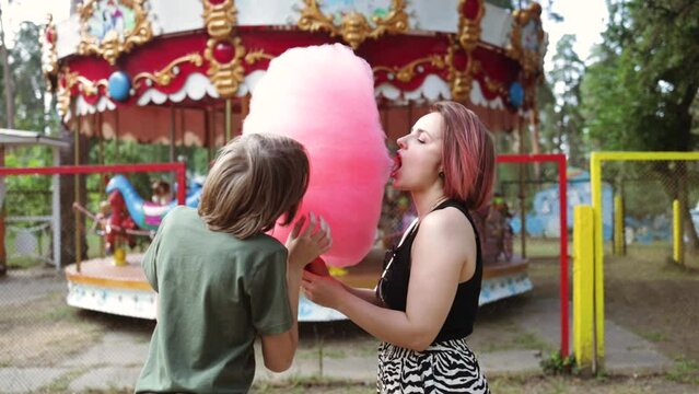 Authentic shot of a happy smiling mother and her little son are having fun to eat together a cotton candy in amusement park.