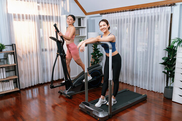 Fototapeta na wymiar Energetic and strong athletic asian woman running on elliptical running machine at home with workout buddy or trainer. Pursuit of fit physique and commitment to healthy lifestyle. Vigorous
