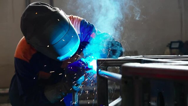 Welding work at a metalworking plant. A helmeted welder welds a metal part on a welding table