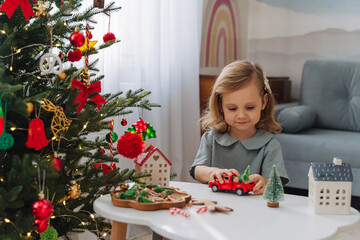 Christmas holidays. A little girl plays with toy cars, little houses and christmas decorations. Holiday Activity for Kids. Merry Christmas and Happy Holidays!