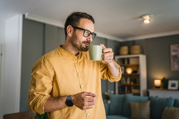 One young caucasian man having cup of coffee while standing at home