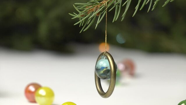 Handmade Christmas decoration from brass ring and glass ball on the spruce branch against the background of spruce tree with Christmas lights, holiday concept.