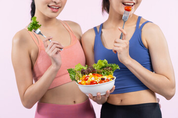 Two young sporty Asian women in sportswear holding salad bowl fill with fruit and vegetable. Natural youthful and fit body lifestyle people with balance nutrition on isolated background. Vigorous