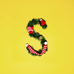 Christmas alphabet. Letter S made of pine tree branches, Christmas ornaments, red knitted hat, gloves and scarf on gold table background. Flat lay, top view, copy space. Christmas composition.