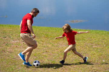 Obraz premium Dad with his little cute son are having fun and playing football on green grassy summer lawn. Football soccer sport concept. Father and son playing football. Father and kid play with soccer ball.