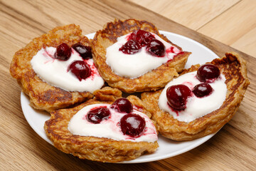 Pancakes are drizzled with creamy sour cream and sweet cherries on a white plate. 