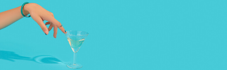 Beautiful groomed womans hand with fashionable ring touch glass of cocktail on blue background