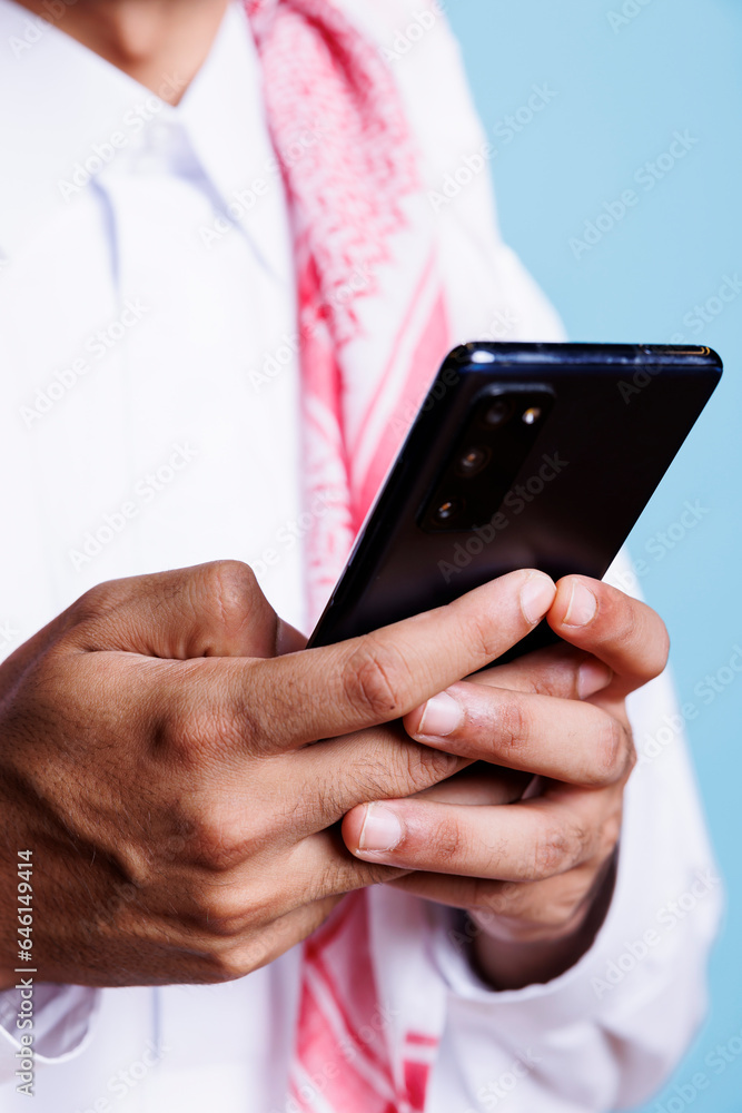 Poster muslim man holding mobile phone in arms, sending online message while using chatting app closeup. ar
