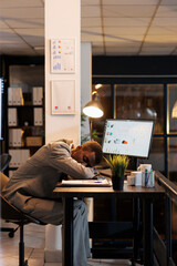 Exhausted manager sleeping on desk table in startup office after working overtime at company strategy. Tired drained african american employee with burnout syndrome resting at work. Business concept