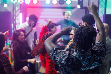 Diverse people dancing and raising hands at discotheque with live music in nightclub. Young clubbers partying, moving to electronic music rhythm and jumping on club dancefloor