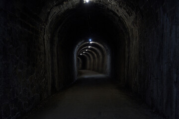 Fototapeta na wymiar stone tunnel dark wet old curved stone illuminated with dirt floor in horizontal