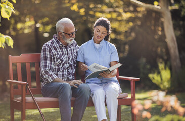 Woman nurse reading book to senior man in park