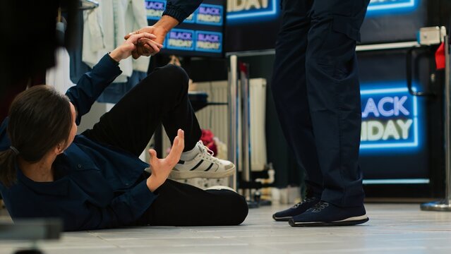 Black friday shopping madness concept. Aggressive shoppers pushing young man on the floor, rushing to enter clothing store. Asian customer getting hurt during seasonal sales event.