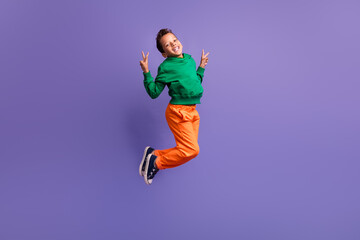 Photo of positive glad boy pupil wear green trendy outfit fly air demonstrate v-sign good mood isolated on purple color background © deagreez