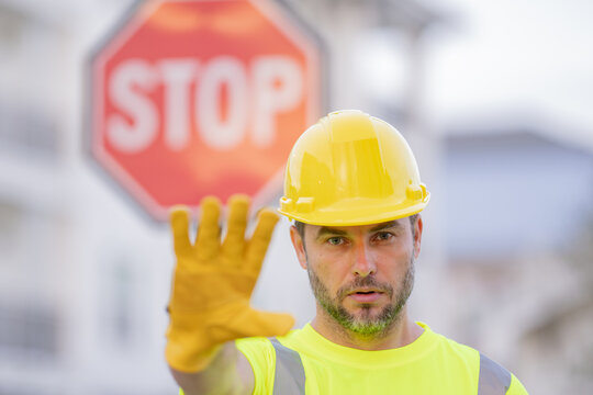 Builder showing STOP. Serious builder with stop road sign. Builder with stop gesture, no hand, dangerous on building concept. Man in helmet showing stop road sign.