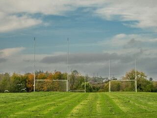 Training pitch for Irish National sport camogie, hurling, rugby and Gaelic football with tall goal posts and freshly cut grass. Nobody. Cloudy sky. Popular activity.