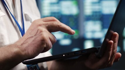 Competent IT professional navigating network of supercomputers in industrial server hub. Expert with laptop ensuring optimal operations, doing optimizations and maintenance in data center, close up