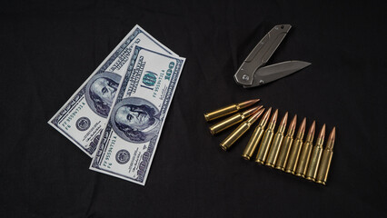 money, a knife, and bullets on a dark cloth