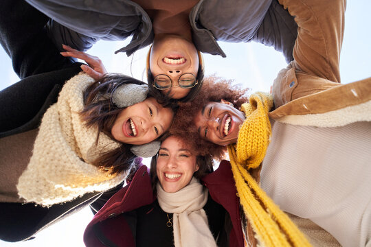 Low angle selfie of group of friends hugging in circle looking at camera excited, happy and smiling. Young cheerful student people posing funny for photo outdoor. Winter vacations and generation z.