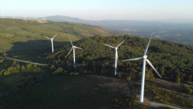 aerial view of eolic generators spining on the top of a hill at sunset