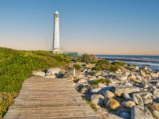 Slangkop Lighthouse , wooden walkway and beach stones on a clear afternoon, Kommetjie, Cape Town, South Africa