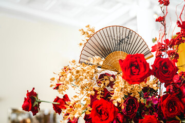 Floral arrangement, festive bouquet, table decoration for Chinese New Year party celebration in restaurant. Traditional red gold color decor. Roses,poppies,fan,candles,tassels. Chinese lunar calendar
