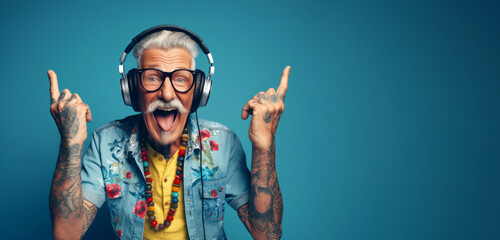 A happy hipster and cool grandfather, original style and tattoos, wearing headphones enjoying music, pointing his fingers up. Active and fun lifestyle concept for seniors: Sunset of life in colors - obrazy, fototapety, plakaty
