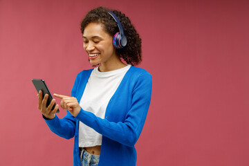Fototapeta Smiling woman listen music in earphones standing on red studio background. High quality photo obraz