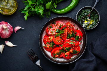 Summer vegan tomato salad with parsley, garlic, pepper and olive oil dressing, black table background, top view