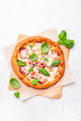 Homemade pizza with italian salami sausage, mozzarella cheese, tomato sauce and green basil on white kitchen table background, top view