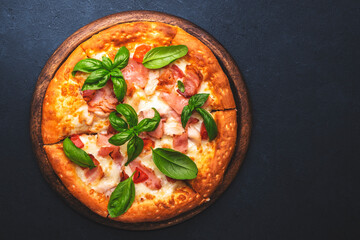 Homemade hot pizza with ham, mozzarella cheese, tomato sauce and green basil, black table background, top view