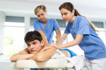 Obraz premium Young man enjoying massage while two skilled female therapists working in tandem to provide relaxation and relief to him muscles ..