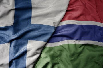 big waving national colorful flag of finland and national flag of gambia .