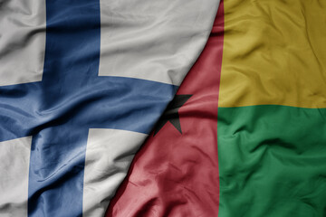 big waving national colorful flag of finland and national flag of guinea bissau .