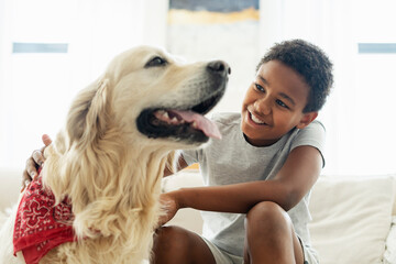 Portrait of smiling boy stroking and playing with golden retriever dog at home. Pet love concept
