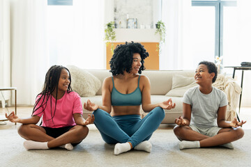 Fototapeta na wymiar Smiling African American mother with son and daughter in sportswear sitting in lotus position