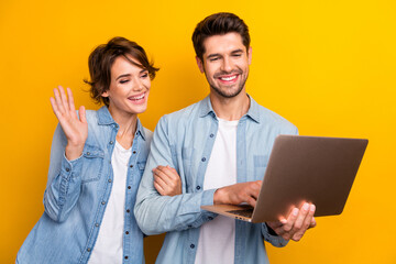 Photo of positive wife nice husband wear stylish denim outfit use wireless netbook speaking waving hand isolated yellow color background