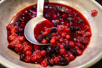 A mixed red, summer fruit compote in a bowl with a serving spoon, part of a self service breakfast buffet at a hotel.