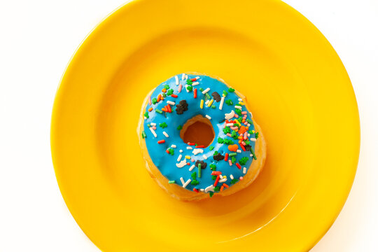 Top view of delicious donut with blue frosting and colorful sprinkles on vibrant yellow plate isolate on white. Sweet desert concept