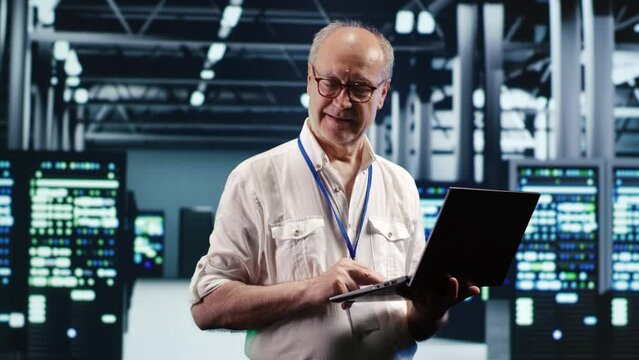 Focused IT professional navigating network of blade servers in industrial hub. Serviceman with laptop ensuring optimum operations, doing optimizations and maintenance in data center
