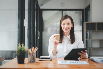 Smiling confident business leader looking at camera and sittingin an office, Portrait of confident businesswoman hand holding coffee cup in boardroom. Using digital tablet during a meeting.