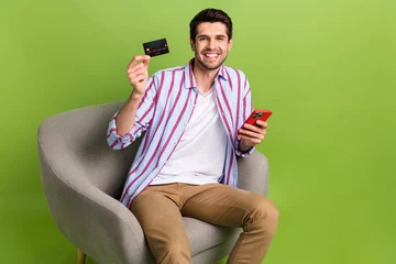 Abwaschbare Fototapete Graffiti-Collage Portrait of toothy beaming person wear stylish clothes sit in armchair hold smartphone debit card isolated on green color background
