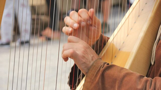 Hands of a man in medieval clothes playing a harp in slow motion close up view